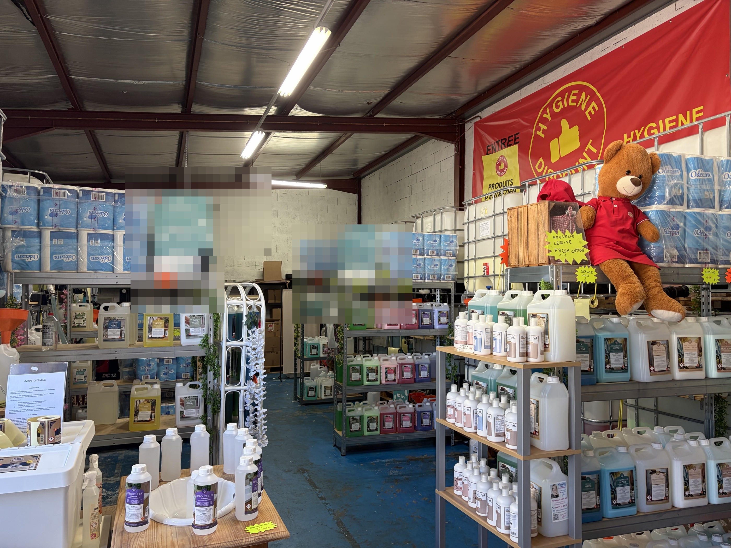 Hall du magasin avec rayonnages de bidons, packs de papier et mascotte ours.